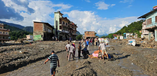 CH11659317 People walk through mud alongside collapsed buildings after the flash flood