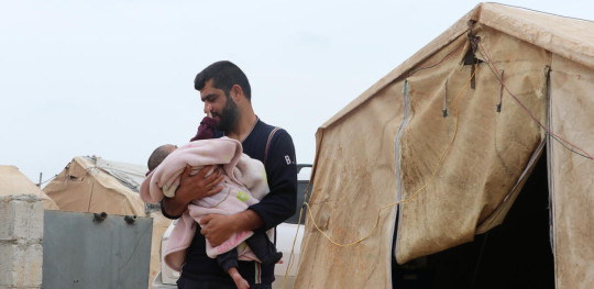 CH1810150 Yanal 44 Carrying his son Emad 10 months outside the tent where the family lives after their home was destroyed by the earthquake in Afrin District Aleppo Governorate Syria