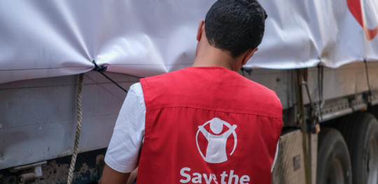 CH1912624 Save the Children staff adjust tarp covering supplies on truck