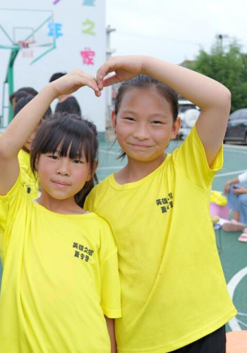 CH1998154 Ying 12 right and her friend Hua smiling at the camera in front of a child care facility v2