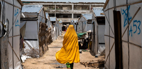 CH1727450 Miriam 16 walks past houses in a camp for displaced people in Borno Nigeria